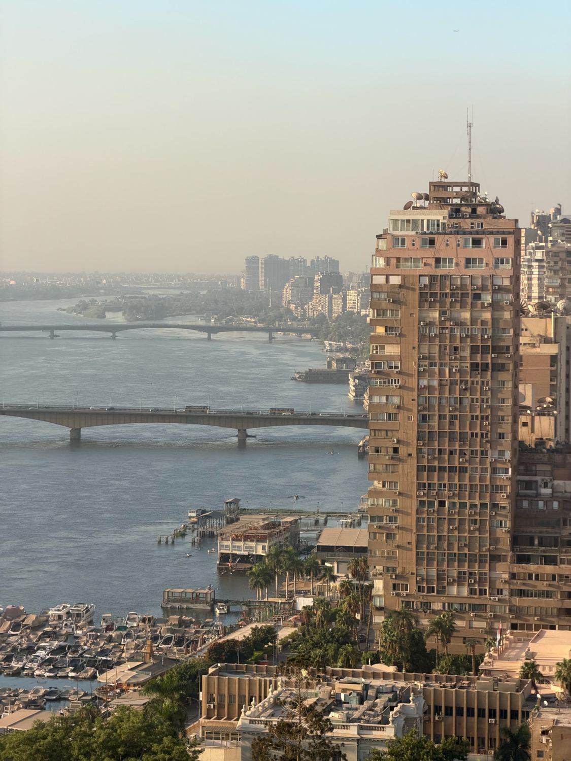 View over the Nile in Cairo with two bridges, houseboats and tall riverside buildings in morning haze