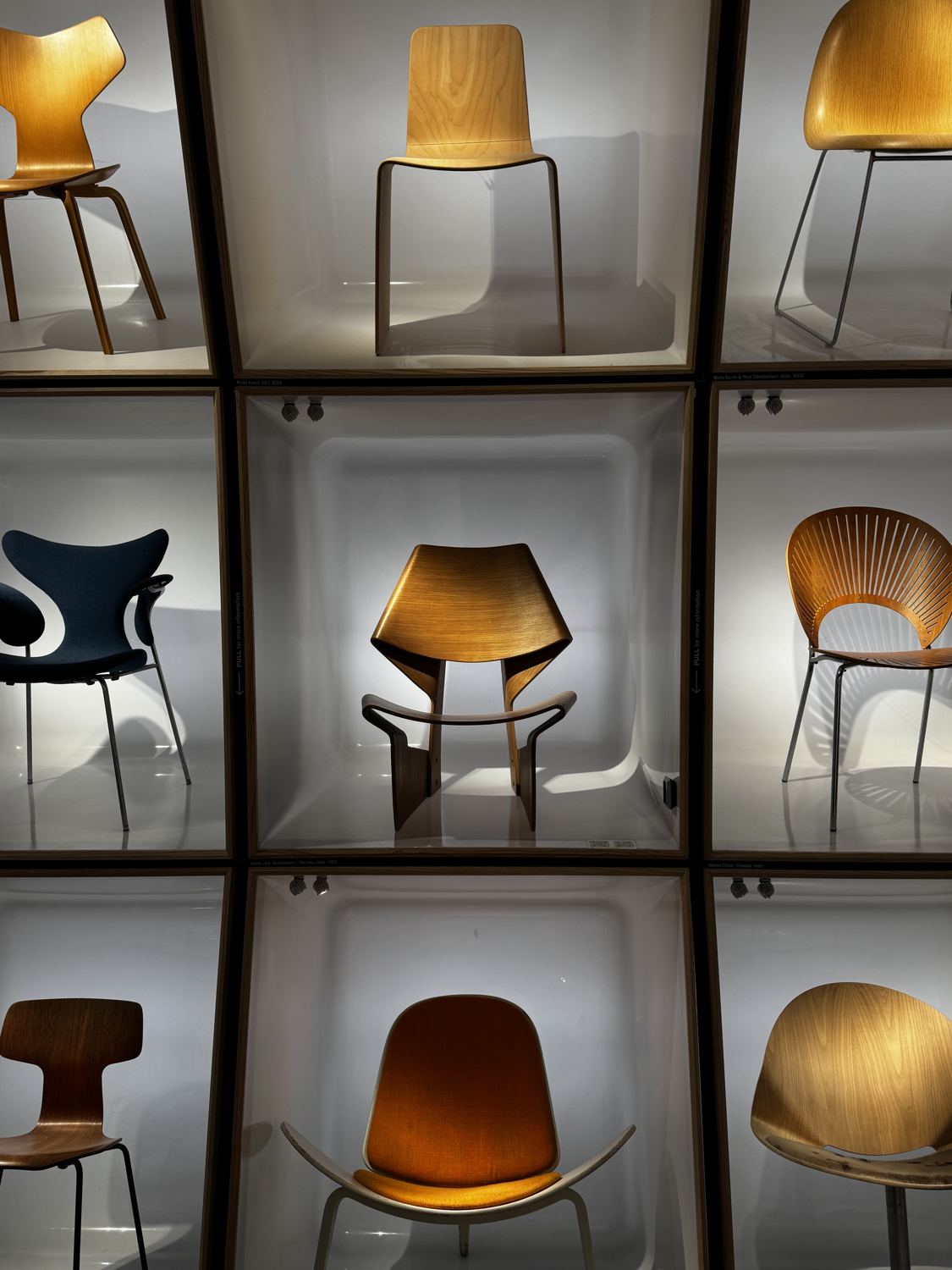 Wall of illuminated display boxes holding classic Danish chairs