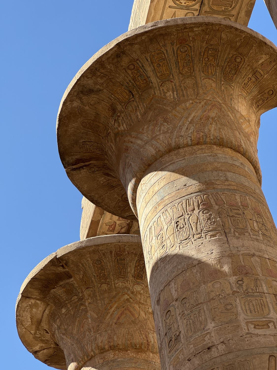 Looking up at painted papyrus columns covered in hieroglyphs against a blue sky at Karnak