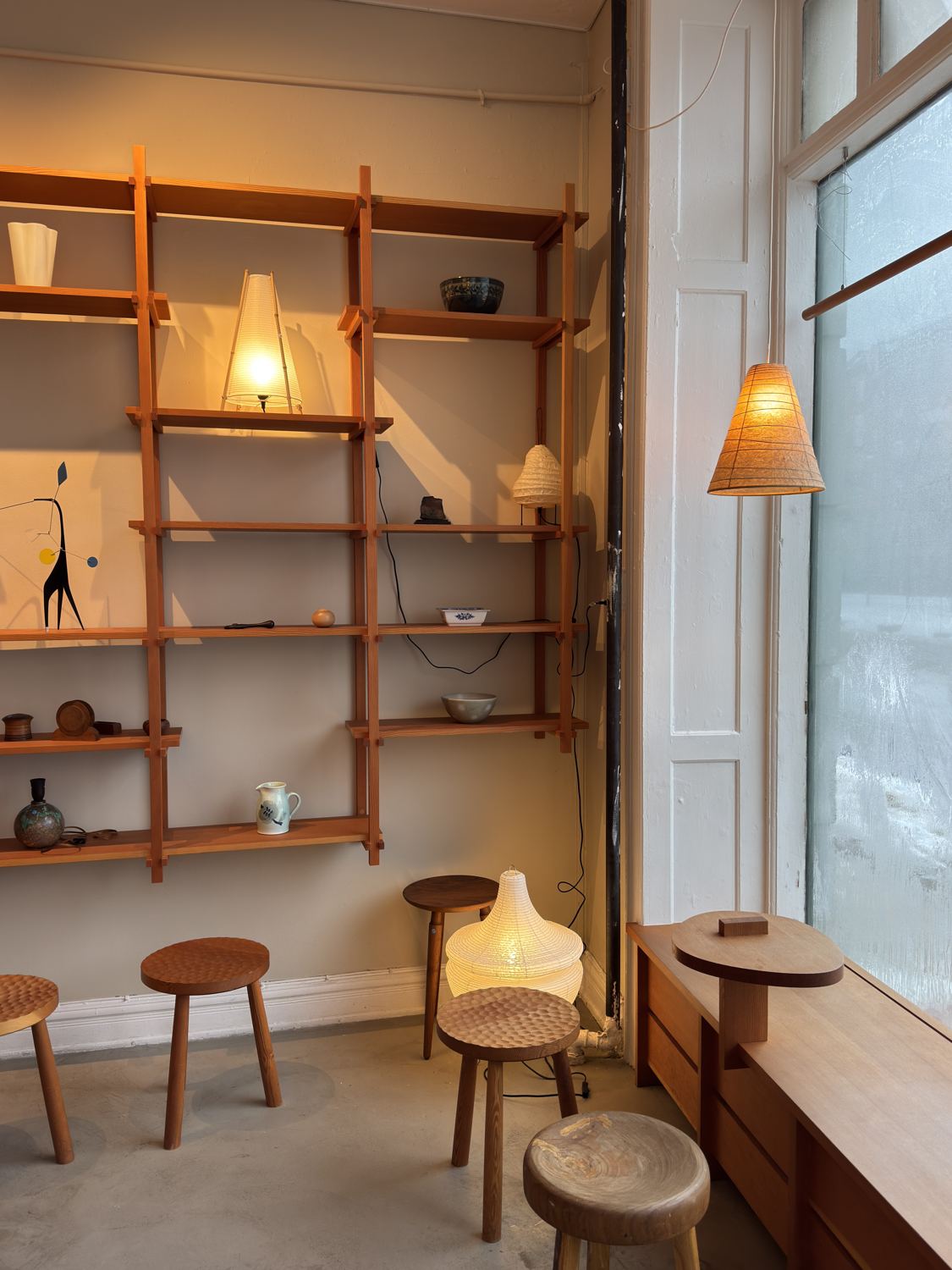 Pine shelving with paper lamps, ceramics and wooden stools in a softly lit room