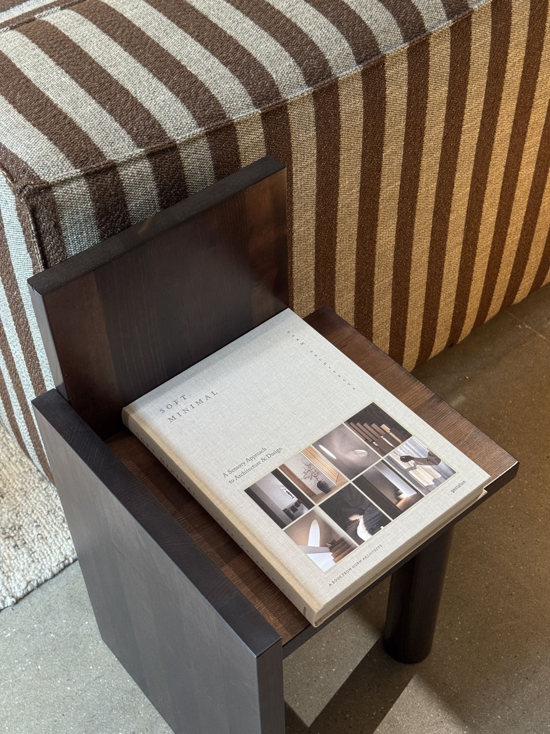 The book Soft Minimal on a dark wooden side table next to a striped sofa